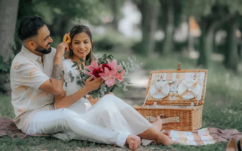 A beautiful couple sitting in a garden under a tree where the man is putting a sunflower on girl's hair